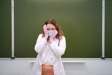 Weary doctor in face mask in school classroom, copy space. School education during the coronavirus epidemic