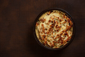 Mushroom and meat casserole covered with melted cheese and served in a dark dish on the table