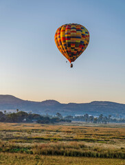 Colourful hot air balloon flying over a grass field during sunrise in Magaliesburg, Gauteng, South Africa
