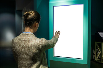 Woman using white blank interactive touchless vertical display of electronic multimedia kiosk with...