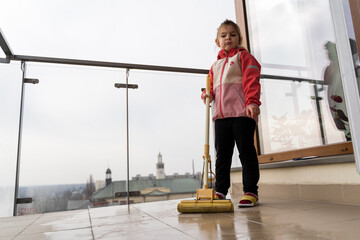 Preschool age girl cleaning balcony floor with mop. Spring cleaning concept