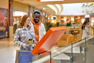 young attractive man and woman using digital navigation board to search information about shops,...