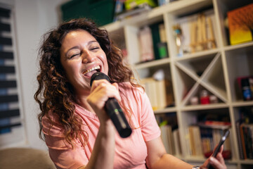 Happy woman singing karaoke at home.