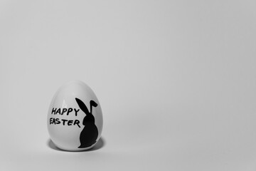 Osterei, weiß, schwarzer Aufdruck, Hase, Happy Easter, Hintergrund grau, Platz für Text, close up