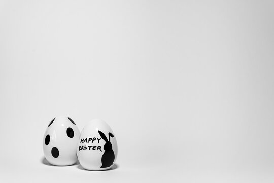 zwei Porzellan Ostereier, wei&szlig;, schwarzer Aufdruck, Osterhase, Happy Easter, Punkte, Hintergrund grau, Platz f&uuml;r Text