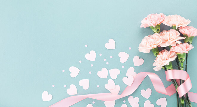 Happy mothers day composition. Pink carnation flowers and paper hearts on pastel blue background top view. .