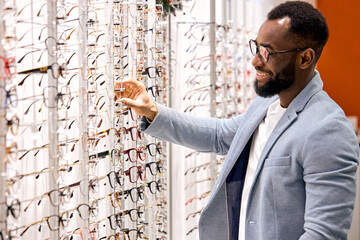 Handsome young smiling bearded african man buying eyeglasses at optics . Consumerism, shopping,...