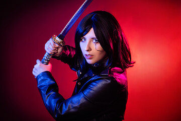 Portrait of a young woman with a bob hairstyle in a black leather jacket with a katana in her hands posing isolated on a dark background with red backlights, cyberpunk concept.