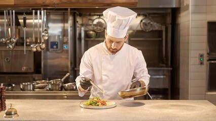 Portrait of skillful professional caucasian chef in white uniform and gloves decorating delicious salad adding shrimps. Handsome cheerful male cook with beard enjoying cooking at kitchen.