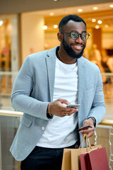 Happy smiling handsome young bearded man holding smartphone, card and colorful shopping bags.happiness, man buying goods online, close up side view photo.shopping addiction.