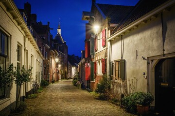 Narrow cobblestone alley between brick buildings in a town under blue evening sky