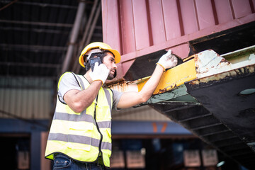Caucasian warehouse worker in uniform with hard hat using mobile phone checking and inspection...