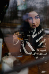 The girl with dark hair is drinking tea and tapping on her phone at a morning café at a table where a beautiful bouquet of white flowers is lying