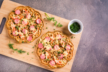 Waffle pizza with tomatoes, sausages, cheese and herbs on a wooden board. Top view