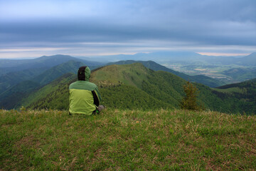 Naklejka na ściany i meble Hiker sitting in grass , on background mountain Osnica , Mala Fatra, Slovakia in spring cloudy morning