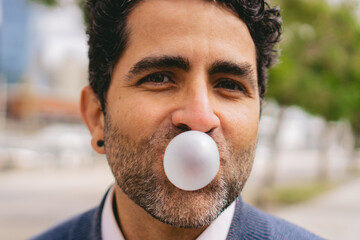 Close-up detail of a middle-aged man blowing a bubble with chewing gum while looking at the camera.