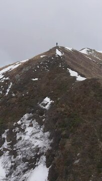 Aerial shot o a hiker walking on the top of the mountain during snowfall