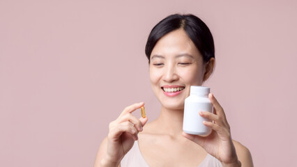 Portrait young asian woman happy smile face with vitamin nourishment pill. Pretty cute girl female person holding health capsule supplement skin care isolated on pink background. Medication concept.