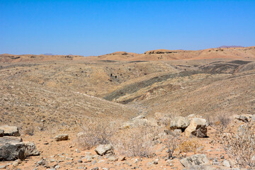 Arid desert hills with rocks all the way to the horizon against a blue sky background