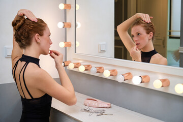 Young ballerina fixing her hair into a bun using bobby pins.