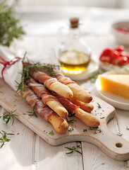 Bunch of traditional italian Grissini breadsticks wrapped parma ham, prosciutto di parma with fresh herbs on a wooden board, close up view 