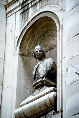 Vertical shot of a stone bust under an arch on a building in Venice, Italy