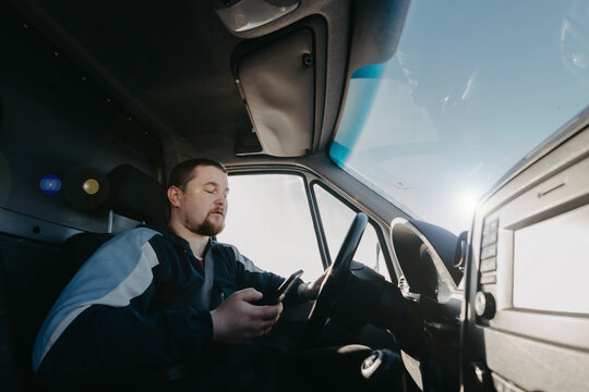 male truck driver with a smartphone in his hands is driving, shipping.