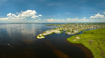 Obraz premium Aerial view of residential suburbs with private homes located near wildlife wetlands with green vegetation on sea shore. Living close to nature concept