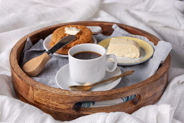 round wooden tray with butter, oatmeal cookies, cup of black coffee, breakfast in bed