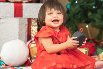 Happy Caucasian cute little girl enjoy music on a bluetooth speaker, sitting on floor near big gift...