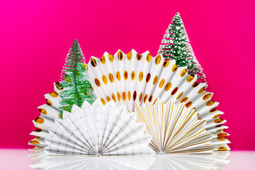 White table with paper fans and new year trees on magenta background with space for product presentation. Christmas and New Year holiday background for display of advertising products