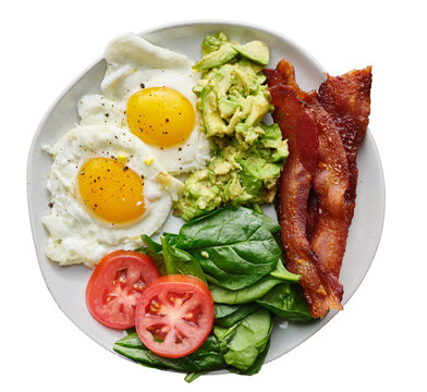 isolated keto friendly low carb breakfast plate with sunny side up eggs, mashed avocado, bacon strips and spinach shot from top view
