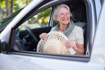 Portrait of attractive smiling senior woman casual dressed entering the car holding her hat