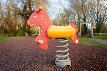 Colourful children's rocking horse on springs over wood chip floor in outdoor playground with trees.