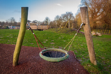 Birds nest children's play swing hanging from two wooden pole structures in outdoor playground.