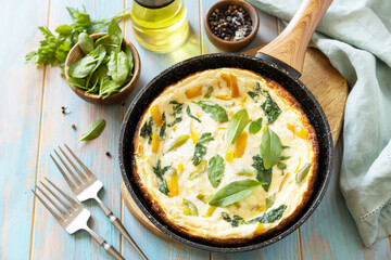 Healthy frittata or stuffed omelette in pan on rustic wooden background. Italian omelette with organic spinach and bell pepper.