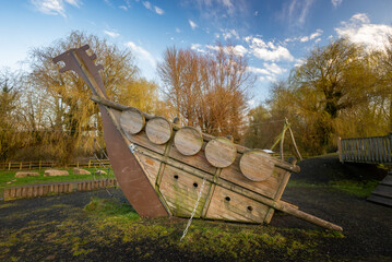 Wooden boat climbing frame structure in outdoor natural public playground with grass and trees.