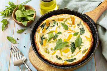 Healthy frittata or stuffed omelette in pan on rustic wooden background. Italian omelette with organic spinach and bell pepper.