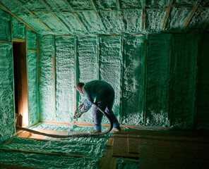 Male builder insulating wooden frame house. Man worker spraying polyurethane foam inside of future...