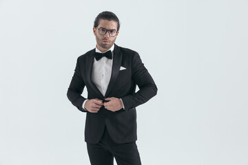 Obraz na płótnie Canvas attractive elegant man with glasses closing and buttoning black tuxedo