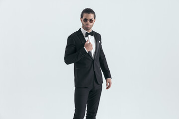 handsome elegant best man in black tuxedo adjusting jacket and posing