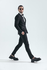 elegant businessman in black tuxedo walking with hands in pockets