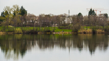 Fototapeta na wymiar City park with cranes symmetrically reflected in lake water