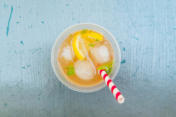 Lemonade with lemon slices, ice cubes and a colorfully striped straw on a blue table, top down view