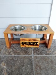 Stainless steel dog water bowls in wooden stand with attached sign Guest