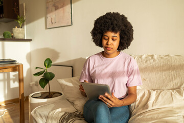 Young Hispanic woman with afro hairstyle wearing pink shirt and jeans in the apartment siting on...