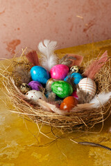 Fototapeta na wymiar Colored Easter eggs and bird feathers in a nest of hay on a yellow background.