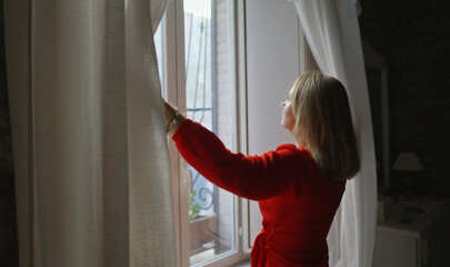 Fototapeta na wymiar Woman opening curtains in her apartment.