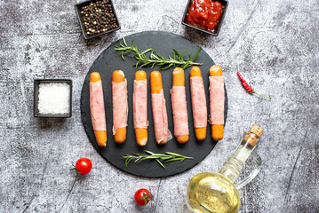 raw sausages wrapped in bacon on a stone background