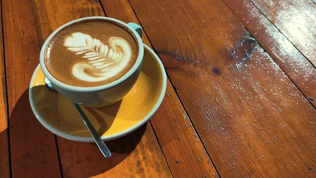 4k clip with speciality coffee cup with art latte depicting a flower served on a yellow table